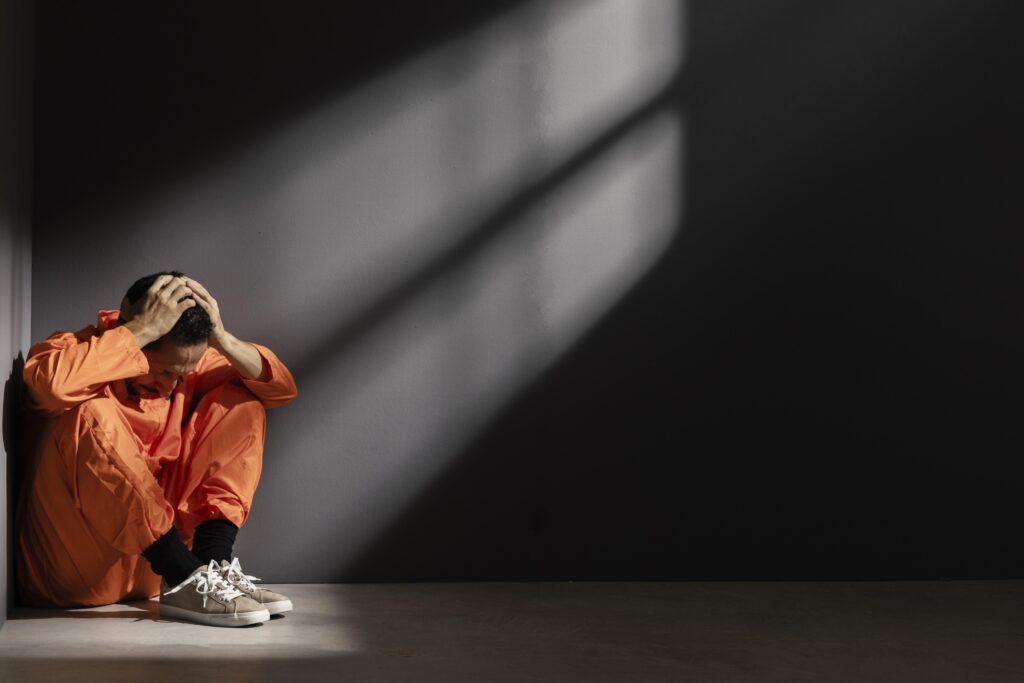 Ansiedade e pânico: quando o medo ganha forma? O homem está sentado no chão, apoiado com o antebraço nos seus joelhos, com as duas mãos sobre sua cabeça e olhando para baixo com uma feição depressiva.